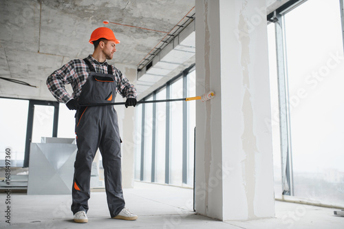 Construction worker painting wall with roller in building under construction