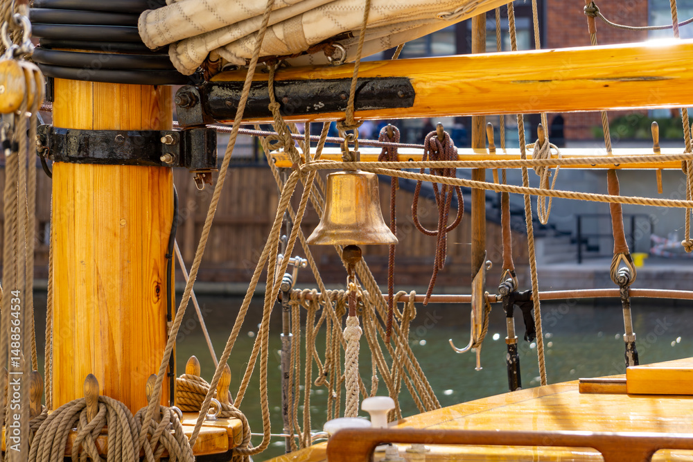 Fototapeta premium close-up of a traditional sailing ship, featuring a wooden mast, rigging, a ship's bell, and deck elements. The warm-toned wood and numerous ropes create a nautical atmosphere, highlighting the crafts