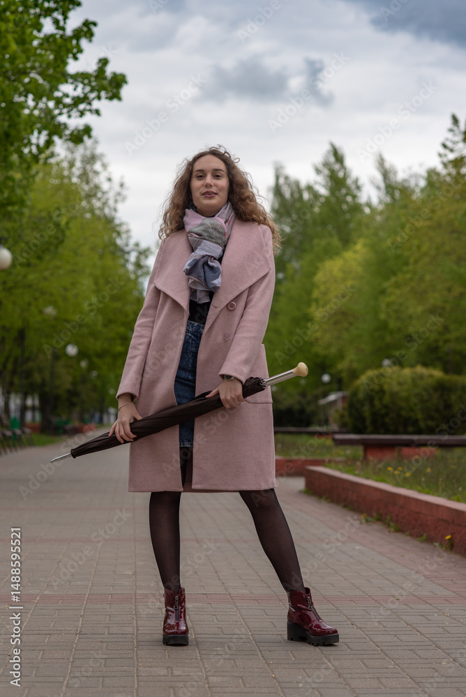 Portrait of a beautiful red-haired girl in a gray coat in a city park.