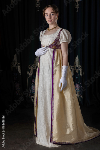 A Regency woman wearing evening attire, including an embroidered dress and a long spencer with gloves