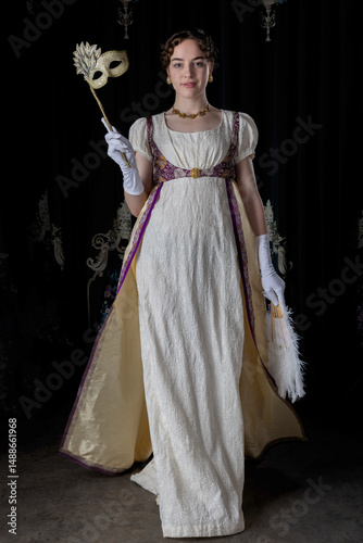 A Regency woman wearing evening attire and holding an ostrich feather fan and a masquerade mask