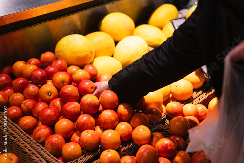 A man chooses Sicilian oranges in a supermarket. A customer buys citrus fruits.