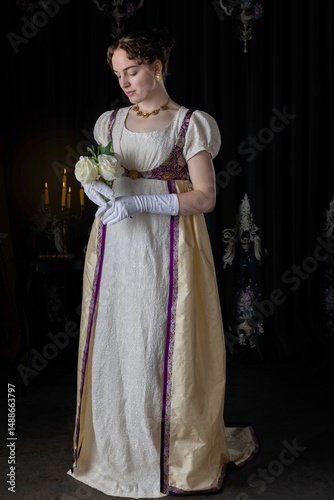 A Regency woman wearing evening attire and standing holding white roses