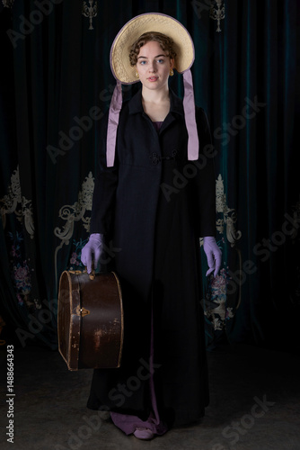 A Regency woman wearing a travelling attire and a bonnet, and standing with a leather hat box