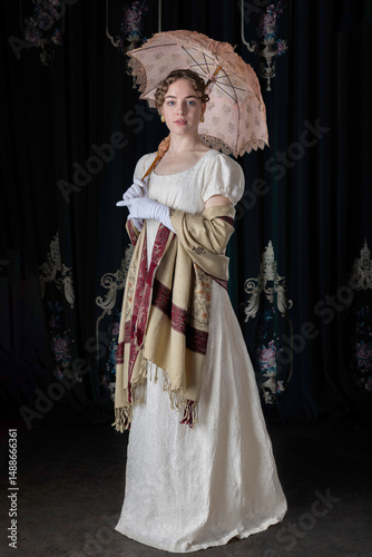 A Regency woman wearing an embroidered dress, shawl, and bonnet standing alone