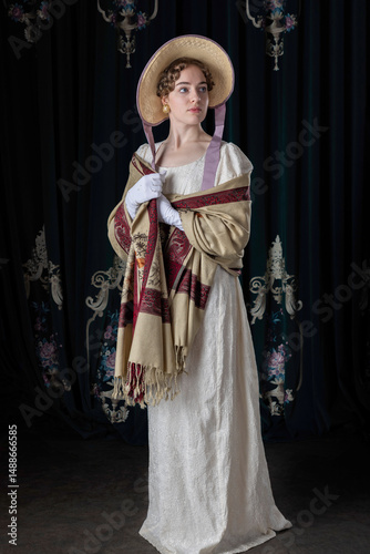 A Regency woman wearing an embroidered dress, shawl, and bonnet standing alone