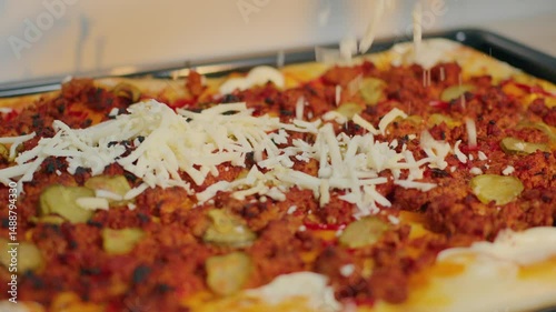 Freshly baked pizza sits on a tray, featuring ground meat, pickles, and sliced peppers