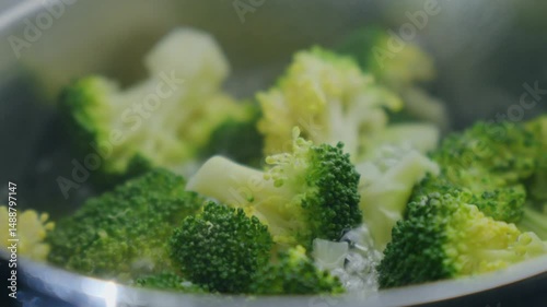 Fresh broccoli florets are submerged in boiling water, bubbling vigorously as they cook.