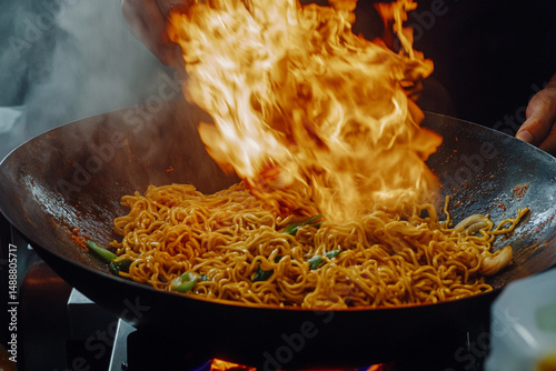 Street food master tosses noodles in a wok, flames scorching the edges of the pan photo