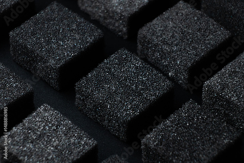 Black Cubes of flexible foam sponges laid out in a pattern. Macro close-up in soft focus. Abstract cubic background