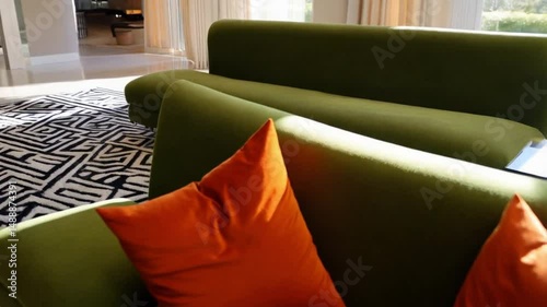 Living room featuring green sofas, orange pillows, and a patterned rug near a bright window