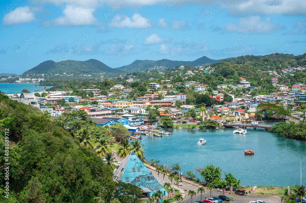 Obraz premium Vibrant aerial view of Castries, Saint Lucia, with colorful buildings, lush hills, calm bay with boats, and tropical landscape under blue sky, perfect Caribbean travel and cityscape (February 2025)
