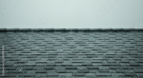 Rain droplets falling on gray shingle rooftop in light storm.