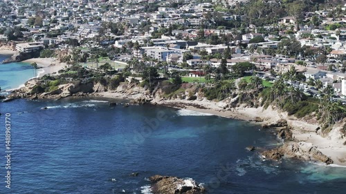 Aerial Panning Beautiful Shot Of Residential Buildings On Cliff In City, Drone Flying Over Wavy Sea During Sunny Day - Laguna Beach, California