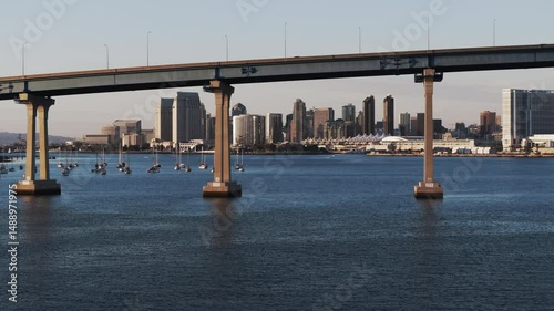 Aerial: Drone Panning Shot Of Cars Moving On Famous Coronado Bridge By Modern Buildings In City Against Clear Sky - San Diego, California