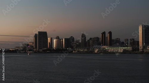 Aerial: Illuminated Modern Buildings In City At Sunset, Drone Flying Forward Over Rippled Sea - San Diego, California