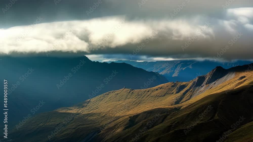 Scenic mountain range with valleys and a thick cloud layer casting shadows, showing a rugged landscape under a partly cloudy sky.