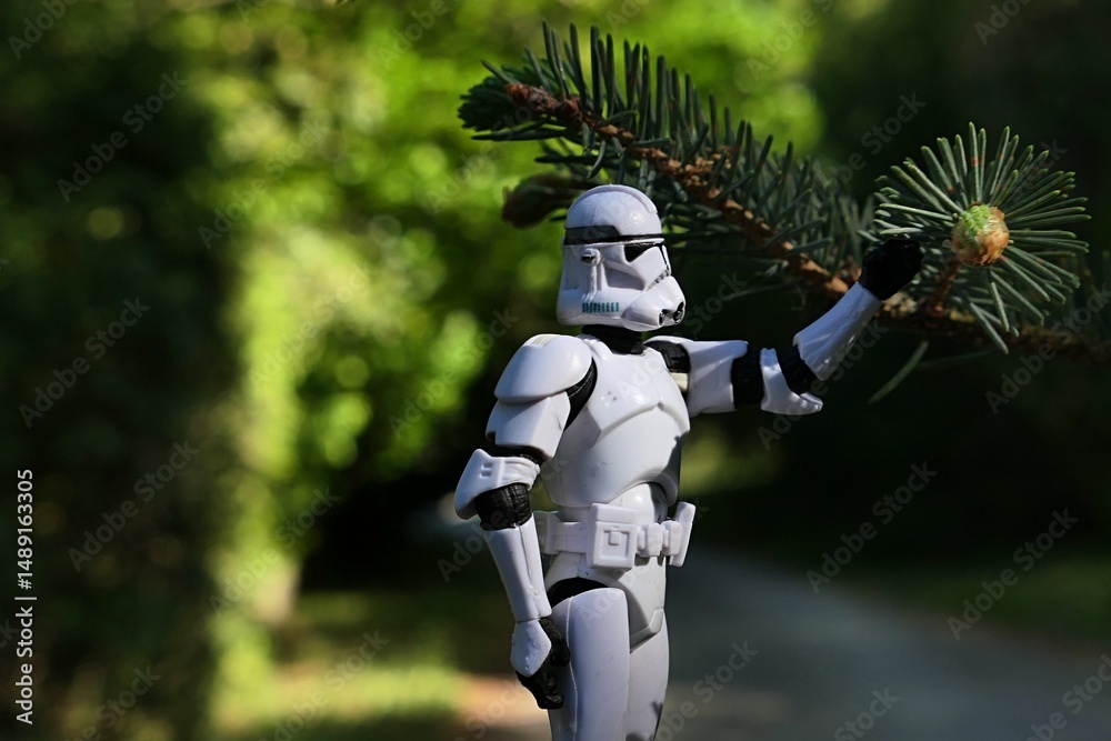 Naklejka premium Star Wars action figure of Clone Trooper examining spring branch tip of coniferous tree Alcock Spruce, latin name Picea alcoquiana. Sunlit by spring daylight sunshine. Park footpath and lawn behind.