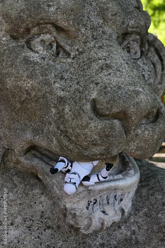 Naklejka premium Large ancient stone statue of lions head chewing figure of Star Wars clone trooper. 