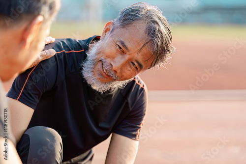 Fotografie Supportive senior Asian man engaging in a wellness conversation with a friend on a track field