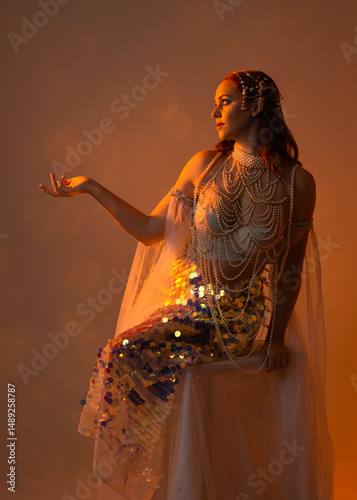 Fantasy studio portrait of a red-haired mermaid faery model wearing white pearl gown, fairytale costume. classical sitting pose facing backwards, ethereal lighting on studio background.
