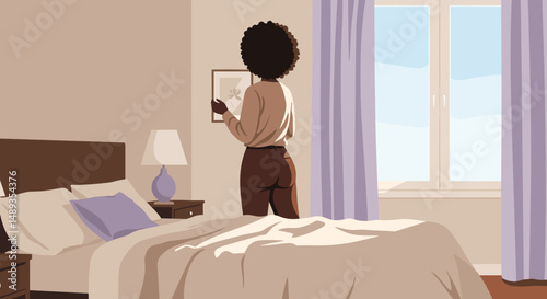 Woman hanging a picture on the wall in a cozy bedroom at home  