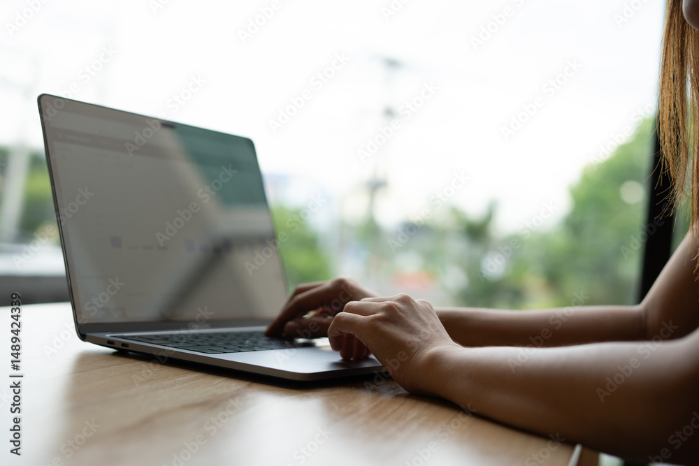 Fototapeta premium Woman's hands typing on laptop keyboard. Freelance or self-employed woman sitting at wooden desk with phone and smartphone.