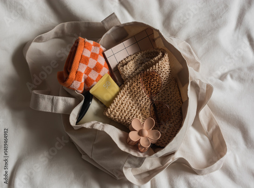 Women's beach accessories - towels, straw hat, book, sunscreen, hair clip in a textile bag on a light background, top view