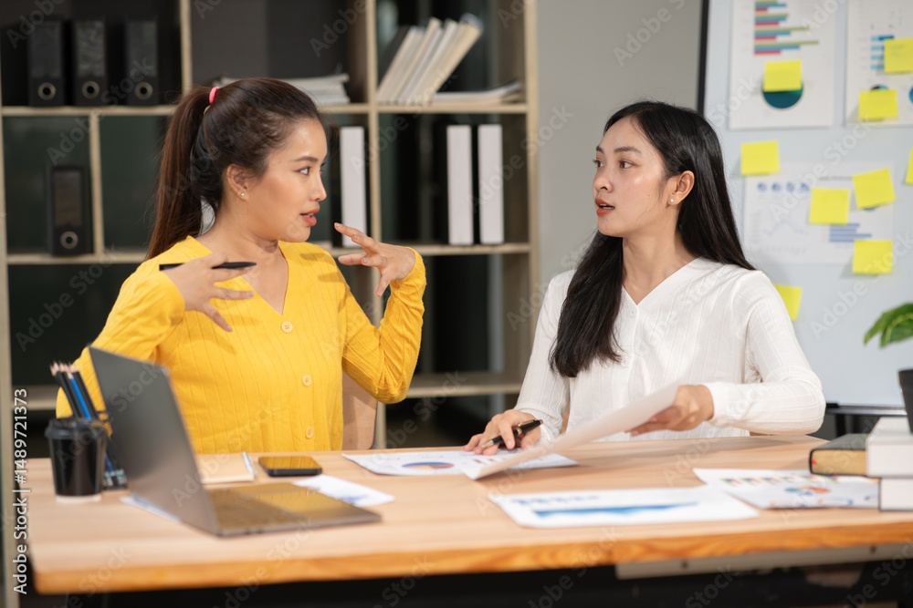 Two Asian businesswomen are sitting in a meeting about planning a chart document in an office. Two Asian businesswomen are sitting in a meeting about planning a chart document in an office.