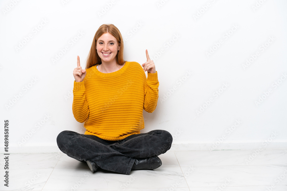 Young redhead woman sitting on the floor isolated on white background pointing up a great idea Young redhead woman sitting on the floor isolated on white background pointing up a great idea