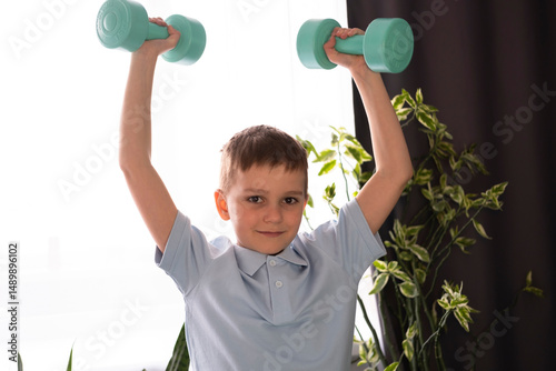 Сute, athletic kid is training with dumbbells. Children's fitness. Activities for children. Sports equipment.