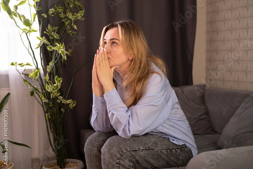 An unbalanced woman is sitting on sofa in living room with her eyes closed, suffering from headaches, dizziness, migraines, cramps in her temples, and needs treatment and rest.