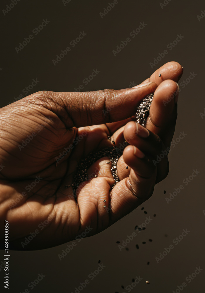 Obraz premium A hand gently pouring chia seeds, creating a beautiful, natural display of texture and light.