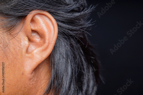 side view of a man's head focusing on the left ear and long hair behind him with a black background for copy space.