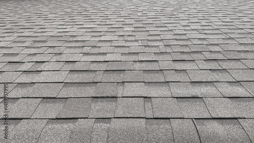 A close-up view of a gray asphalt shingle roof, showing the repeating rectangular pattern and textured surface from a low angle.