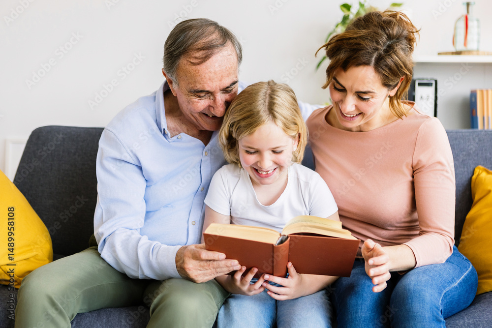 Happy family sharing moments together while reading a book in the cozy living room, creating cherished memories and strengthening bonds Happy family sharing moments together while reading a book in the cozy living room, creating cherished memories and strengthening bonds