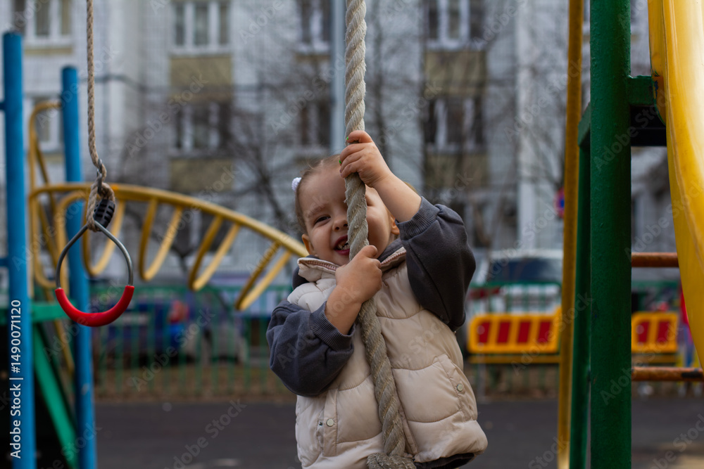 Obraz premium A smiling girl -marsh, rising to a rope on a colorful playground, enjoying classes in the fresh air, developing motor skills and contributing to a feeling of adventure and joy in her childhood.