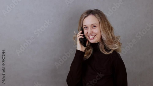 Young attractive woman talking on phone, smiling on gray background