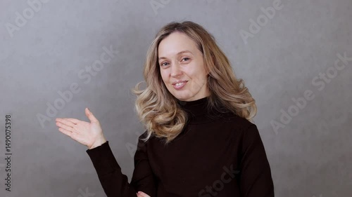 Beautiful young woman on gray background pointing her hand to the side