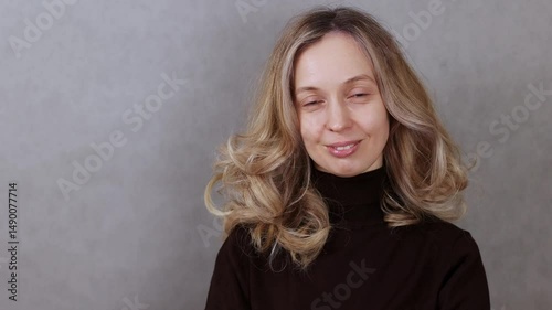 Attractive blonde woman fixing blonde hair on head, gray background and copy space