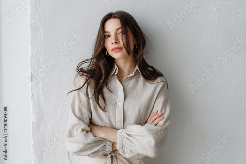 Woman with natural makeup in linen shirt stands against white wall photo