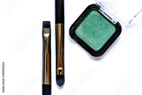 Flat lay of a green eyeshadow palette and two eyeshadow brushes lying parallel on a white background. Creative beauty tools arrangement in soft focus with artistic flair.