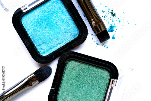Close-up of shimmering green and turquoise eyeshadows with scattered pigments on a white surface. Artistic composition highlighting beauty, color, and creativity.