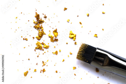 Close-up of scattered gold glitter flakes with a cosmetic brush on a white background. Soft focus enhances the beauty, luxury, and creativity in artistic composition.