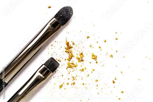 Close-up of scattered gold glitter flakes with a cosmetic brush on a white background. Soft focus enhances the beauty, luxury, and creativity in artistic composition.