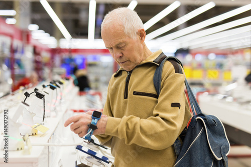 Elderly man examines smart watch in showroom of electronics store