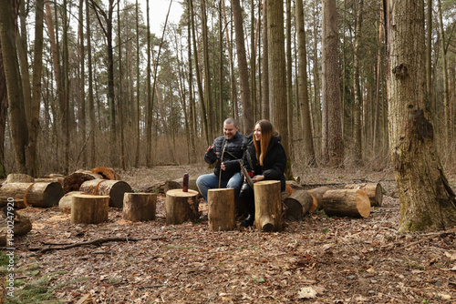 Warm moment between two people enjoying time off the grid, surrounded by tall forest trees, dry leaves, and freshly cut logs that form an improvised seating area