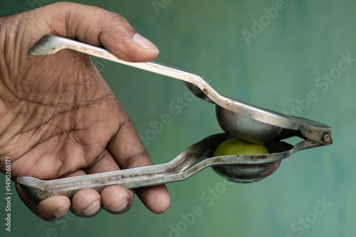 A close-up of a hand holding an old fashioned metal lemon squeezer with a lemon inside, showcasing a rustic kitchen tool commonly used for extracting juice.