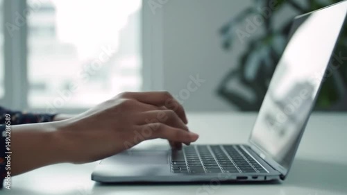 Close-up shot of hands typing on a laptop in a bright and contemporary office setting.