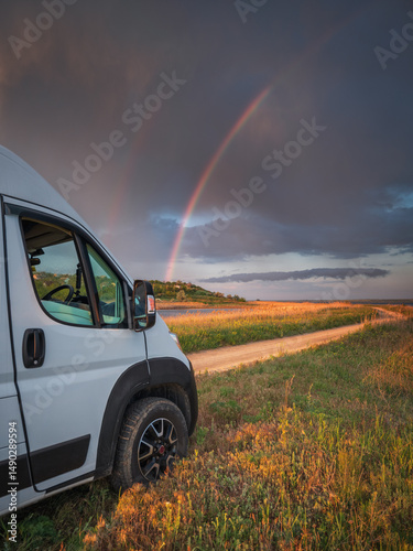 portrait view to head of white van and rainbow in dramatic sky